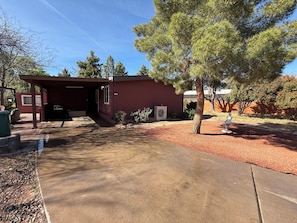 A red building with a covered porch, a concrete driveway, and a tree in the foreground. - Sedona Retreat Walk to Park, Hikes & Sunset Views (Sedona)