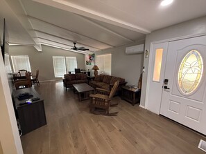 Ein geräumiges Wohnzimmer mit Deckenventilator, ein Essbereich mit Tisch und Stühlen sowie eine Tür mit einem Buntglasfenster.
