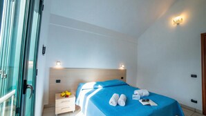 Una habitación de hotel con una cama, una mesita de noche, una pequeña mesa con una lámpara y una puerta.