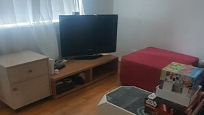 Un salon avec une télévision, une petite table sur laquelle sont posées des boîtes de produits dérivés de Star Wars, un pouf rouge et un meuble blanc.