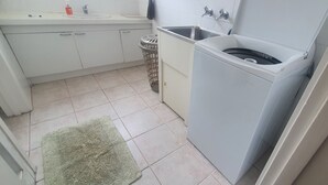 Une cuisine de taille réduite, avec des meubles blancs, un évier, un lave-linge et une poubelle.