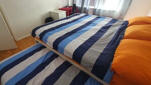 Un lit double avec une literie à rayures, une petite table de chevet, une chaise et une fenêtre avec des rideaux.