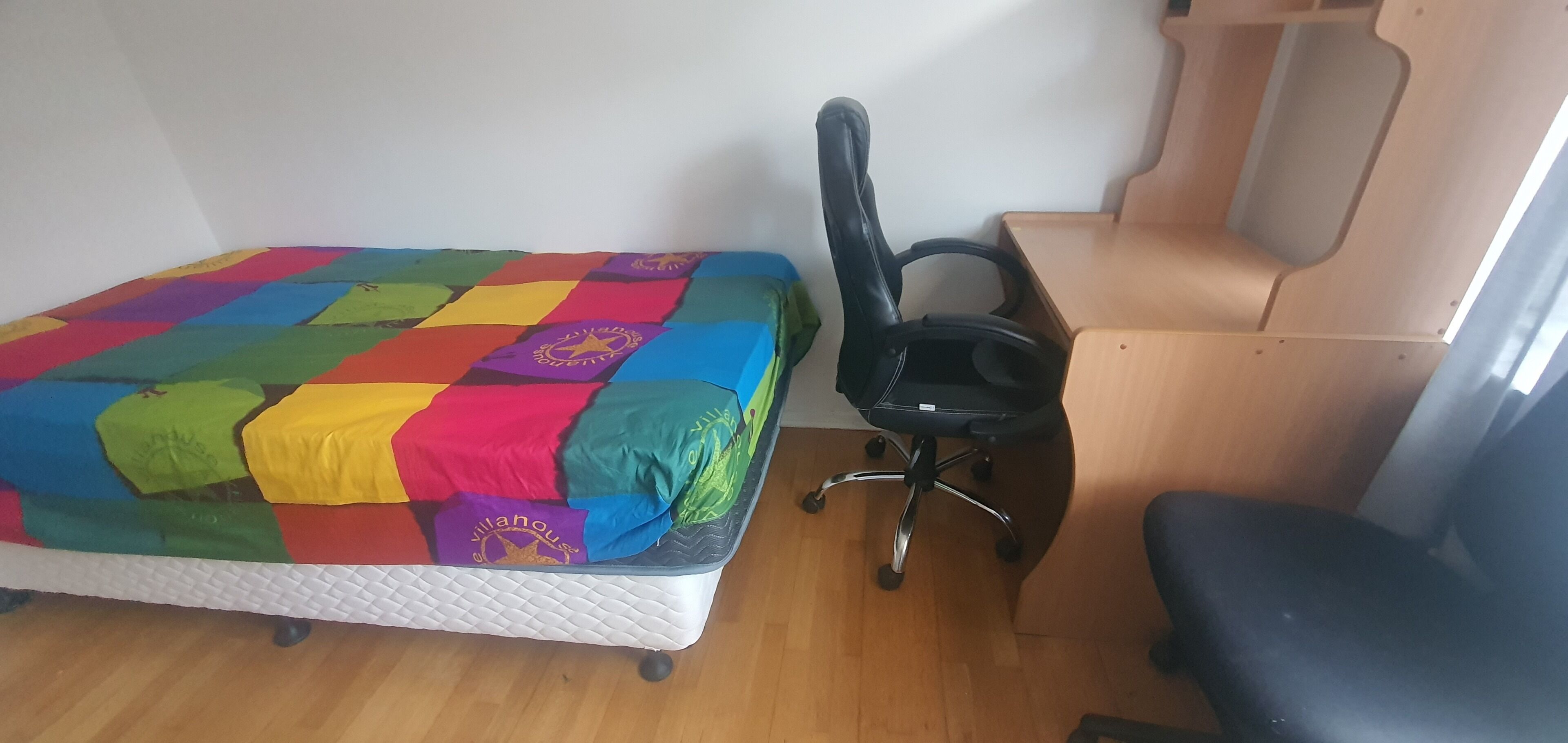 A small room with a bed, a black office chair, and a wooden desk.