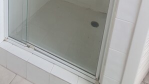 Une cabine de douche fermée par des parois en verre, dotée d’un pommeau de douche à main et d’un robinet fixé au mur.