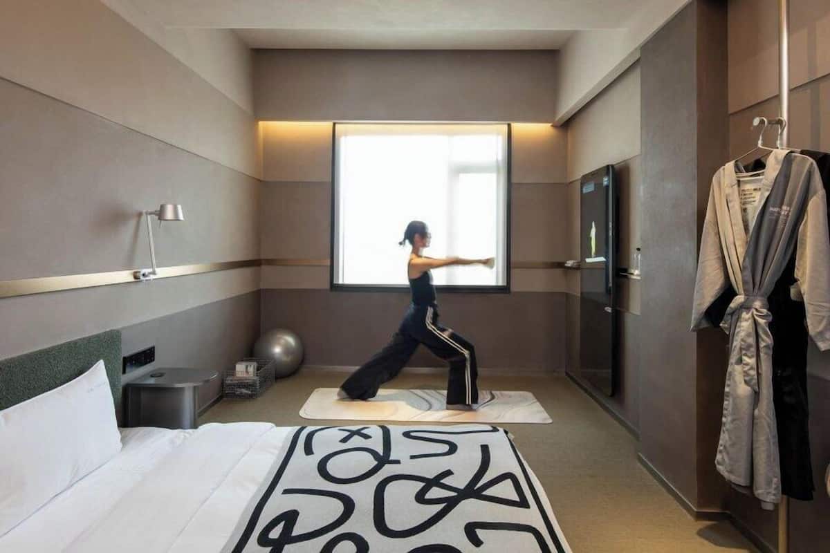 Quarto de hotel com cama, tapete de exercícios, tapete de yoga, bola de ginástica e roupão pendurado na porta.