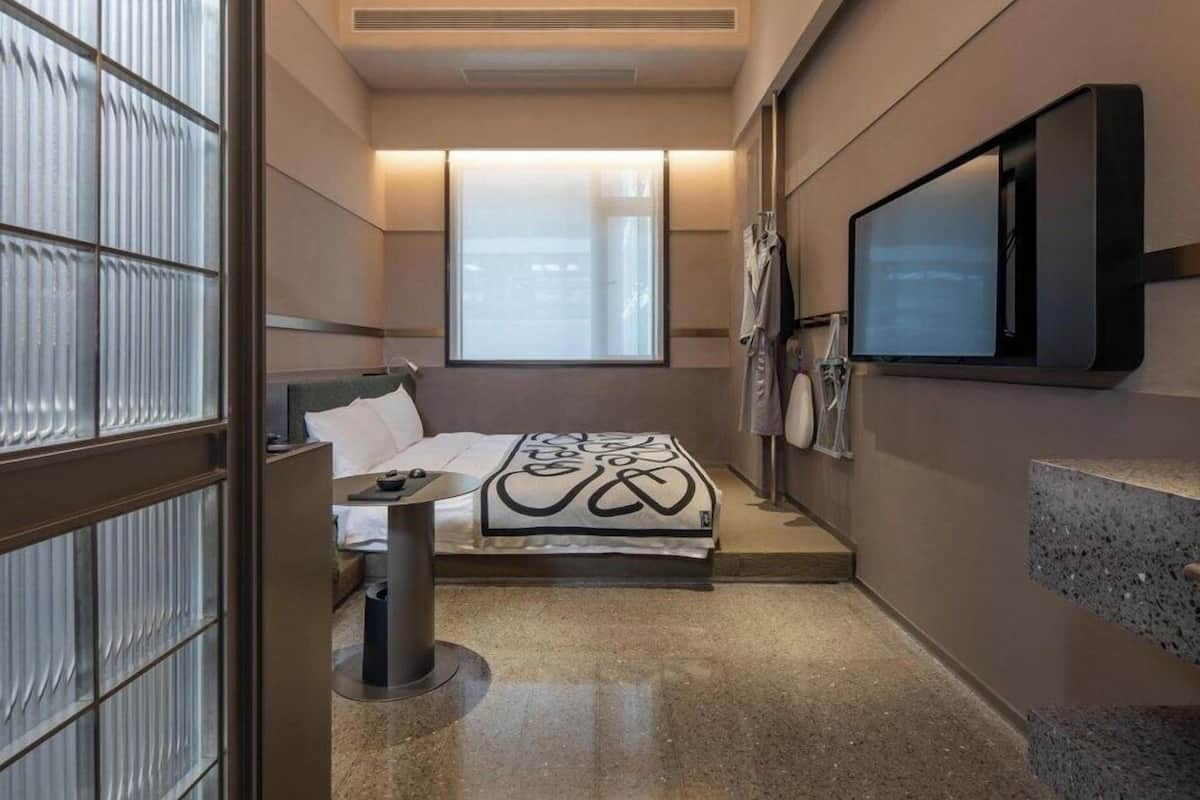 Quarto de hotel moderno com cama, mesa de cabeceira, televisão e janela.