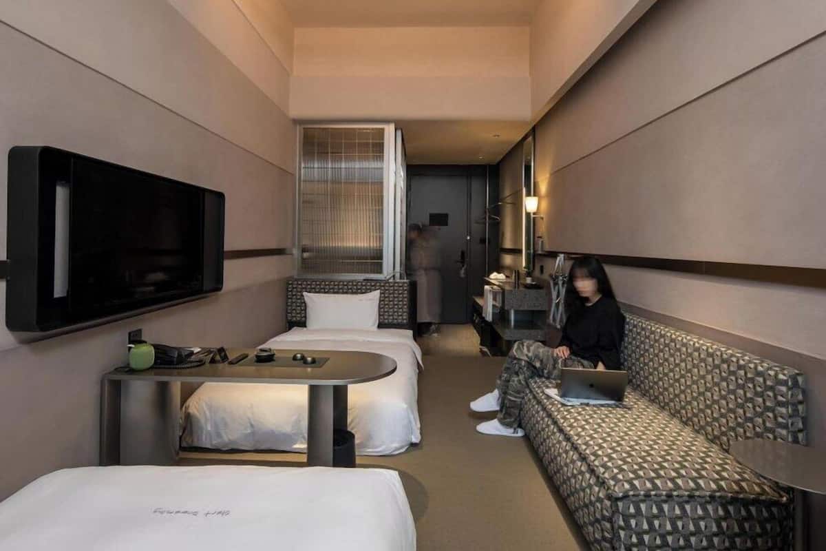 Quarto de hotel moderno com cama, sofá, escrivaninha e televisão.