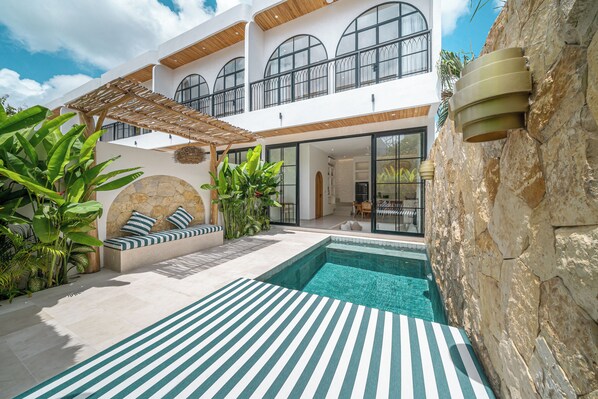 A modern house with a swimming pool, outdoor seating, and a stone wall. - Mareo Villa (Pecatu)