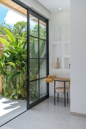 Ein modernes Zimmer mit einer Glasschiebetür, die zu einem Garten führt, einem Holztisch und einem Stuhl.
