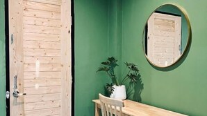 A room with a wooden door, a desk with a chair, a potted plant, and a round mirror on the wall. - Midori Rawai (Rawai)