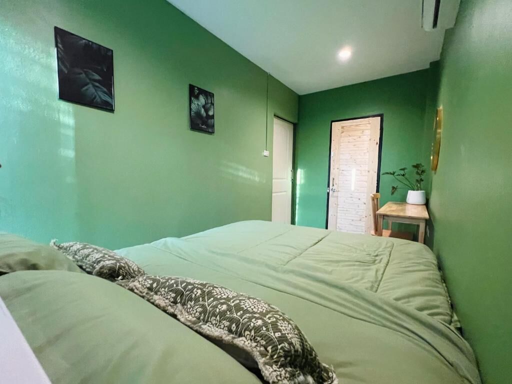 A room with a bed, a small table with a plant, and a door.