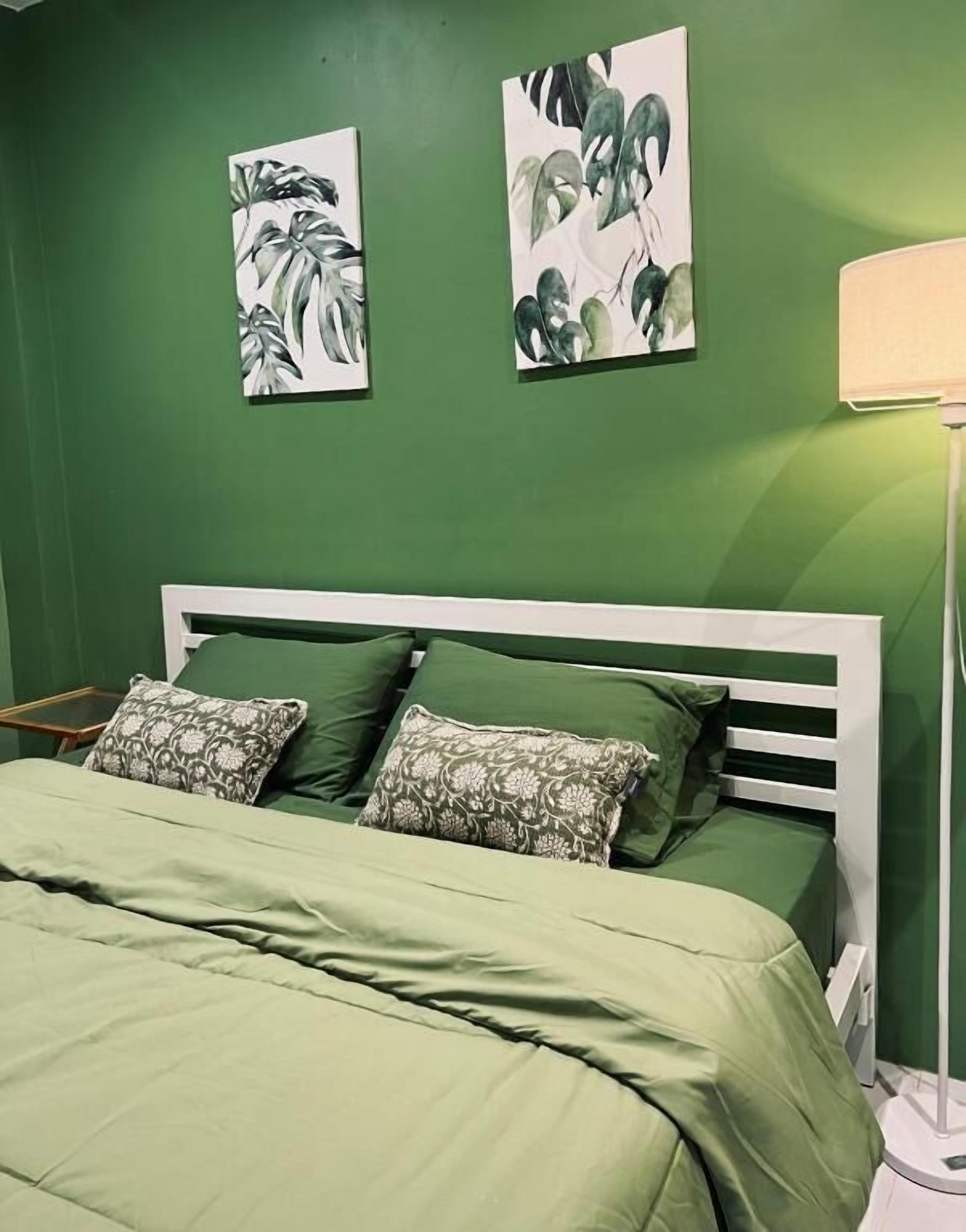 A bed with green bedding, a white headboard, and two wall-mounted paintings.