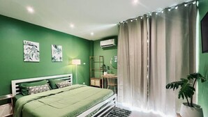 A bedroom with a bed, green walls, a mirror, a plant, and a window with curtains. - Midori Rawai (Rawai)