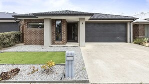 Une maison moderne à deux étages, dotée d’un garage, d’une pelouse bien entretenue et d’un petit jardin.
