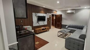 A modern living room with a sofa, coffee table, TV, and a kitchen area with a microwave and coffee machine. - Al Jawhara Park (Riyadh)