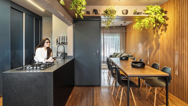 Een moderne keuken met een centraal eiland, een eethoek met een houten tafel en stoelen, en een zithoek met een bank en gordijnen.