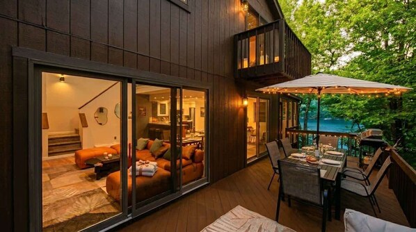 Een modern huis met een grote glazen schuindeur die leidt naar een gezellig woongedeelte met een bank en een eettafel buiten.