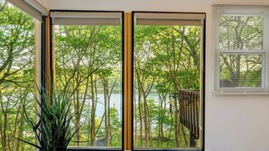 A room with a large window offering a view of a lake and trees. - Lakefront Modern Escape with Hot Tub (East Stroudsburg)