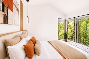 Quarto moderno com cama grande, vista para o verde através de janelas amplas e um quadro na parede.