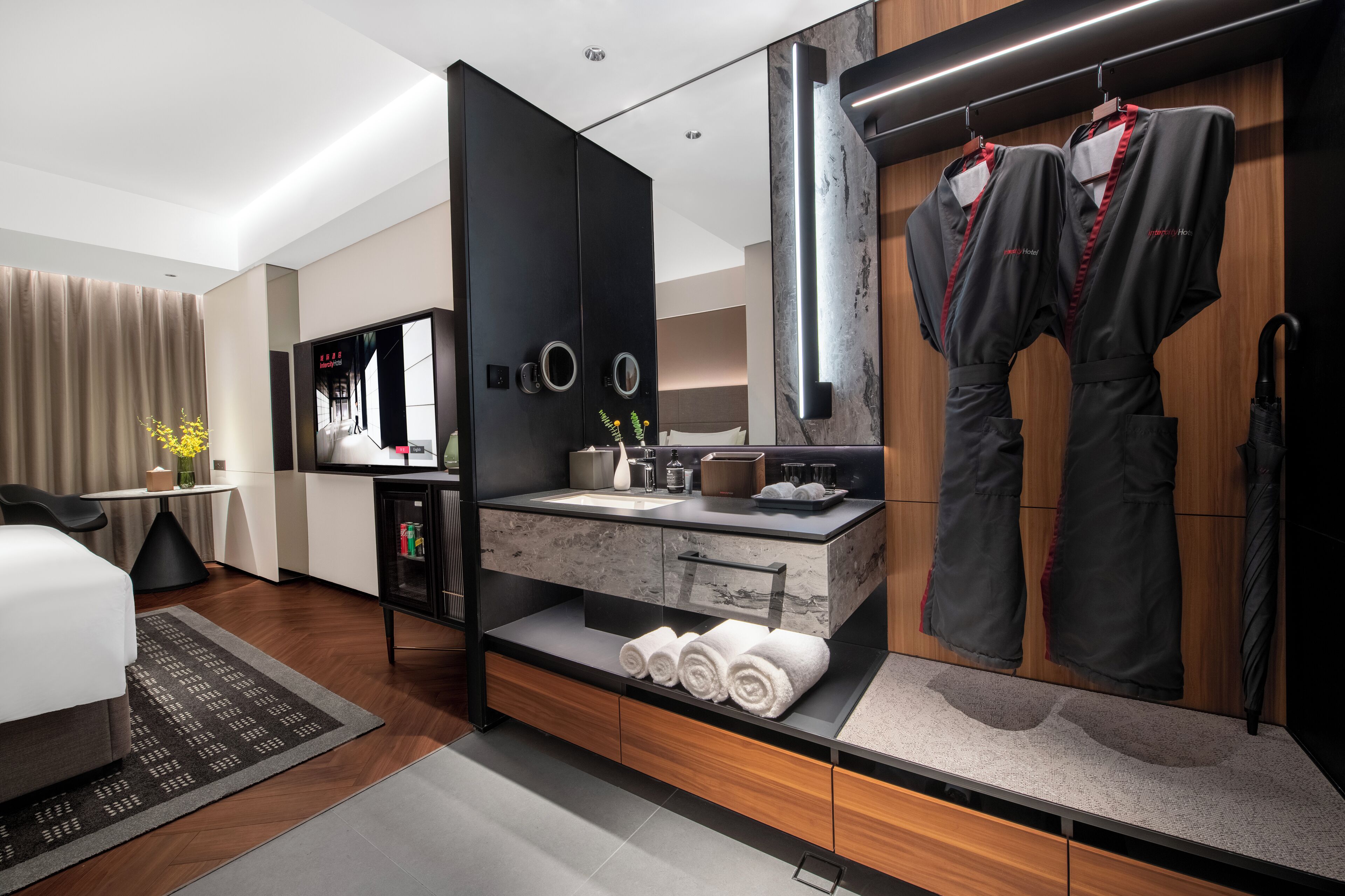 A modern hotel room with a large mirror, a vanity with a marble countertop, and neatly folded towels.