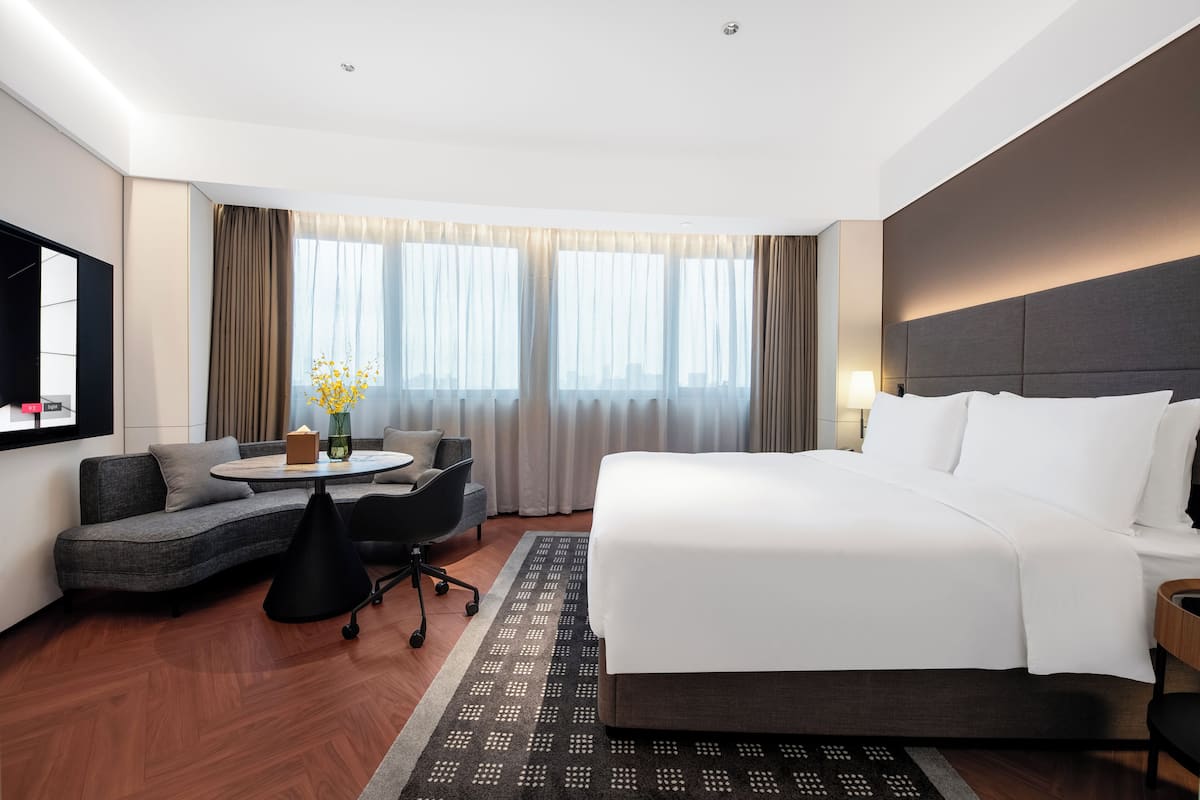 Una habitación de hotel moderna con una cama grande, un sofá, una mesita con un florero y un televisor en la pared.