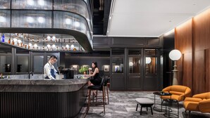 A modern bar area with a curved counter, bar stools, and a seating area with orange chairs and a round table. - Intercity Shanghai Xujiahui (Shanghai)