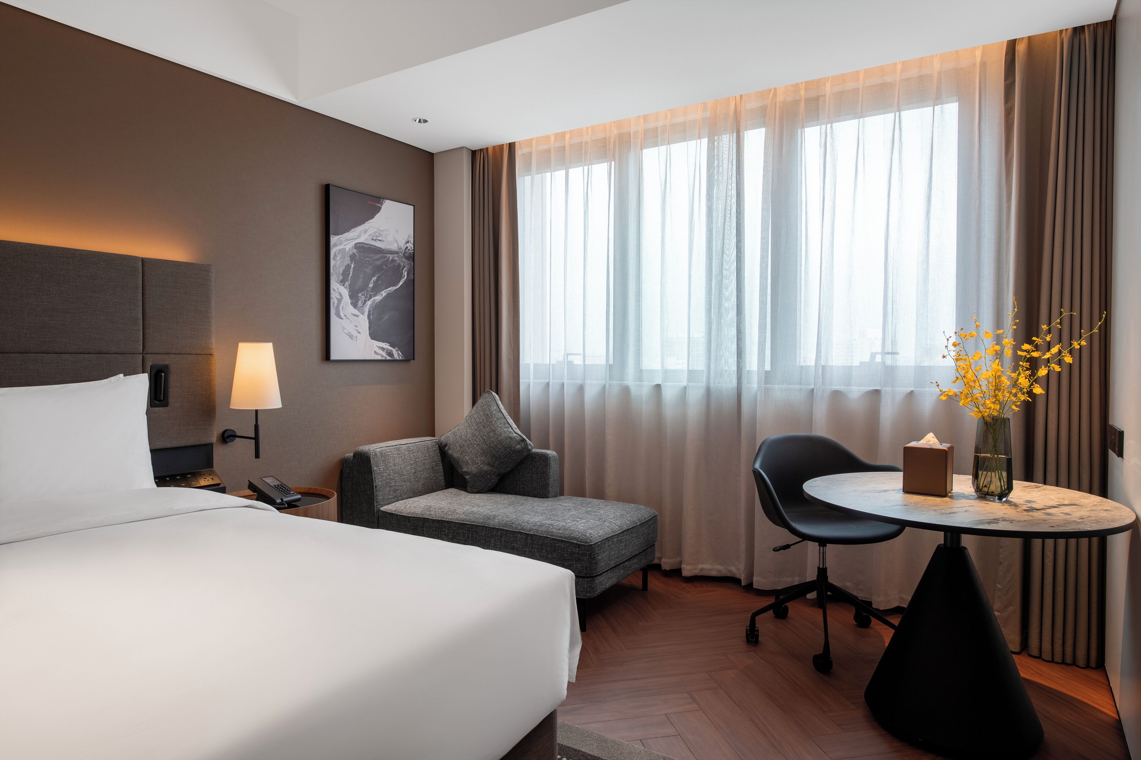 Una habitación de hotel con una cama grande, un sofá, una mesita con un florero y una silla.