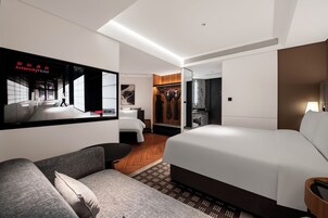 A hotel room with a large bed, a sofa, a TV, a wardrobe, and a mirror.