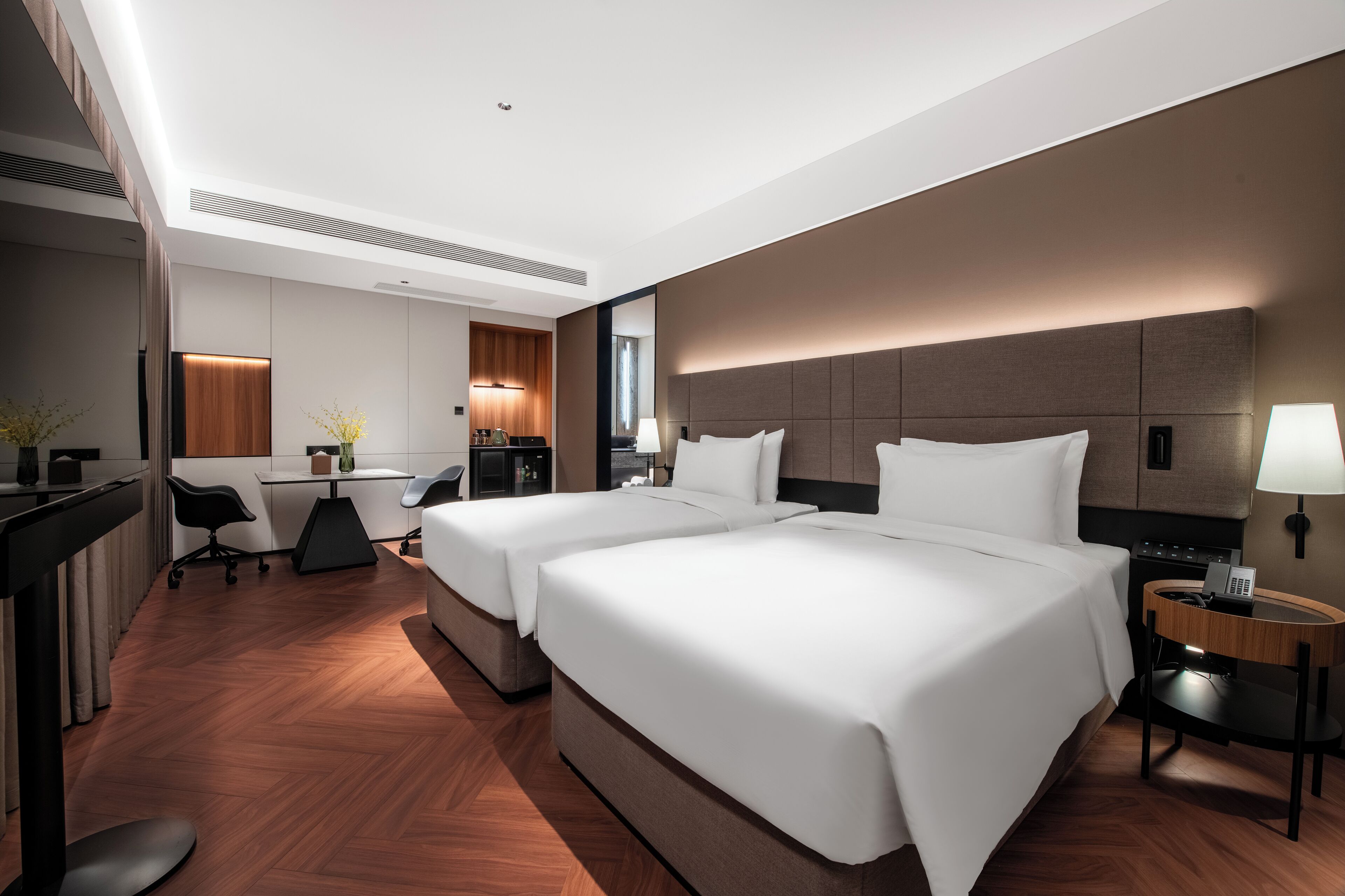 A hotel room with two beds, a desk, a chair, a lamp, and a phone on the side table.
