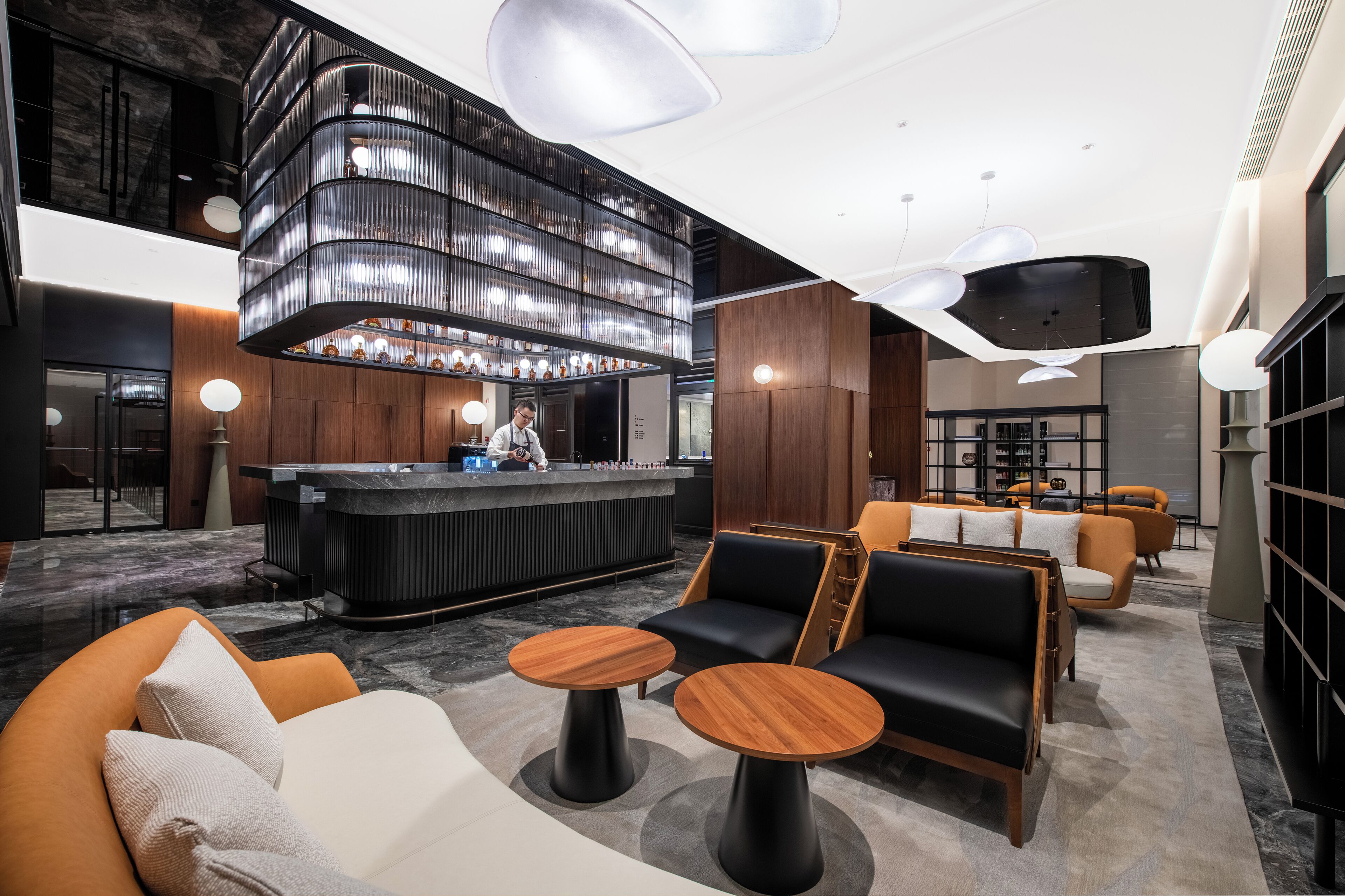 A modern lobby with a curved reception desk, seating area with sofas and tables, and a large chandelier.