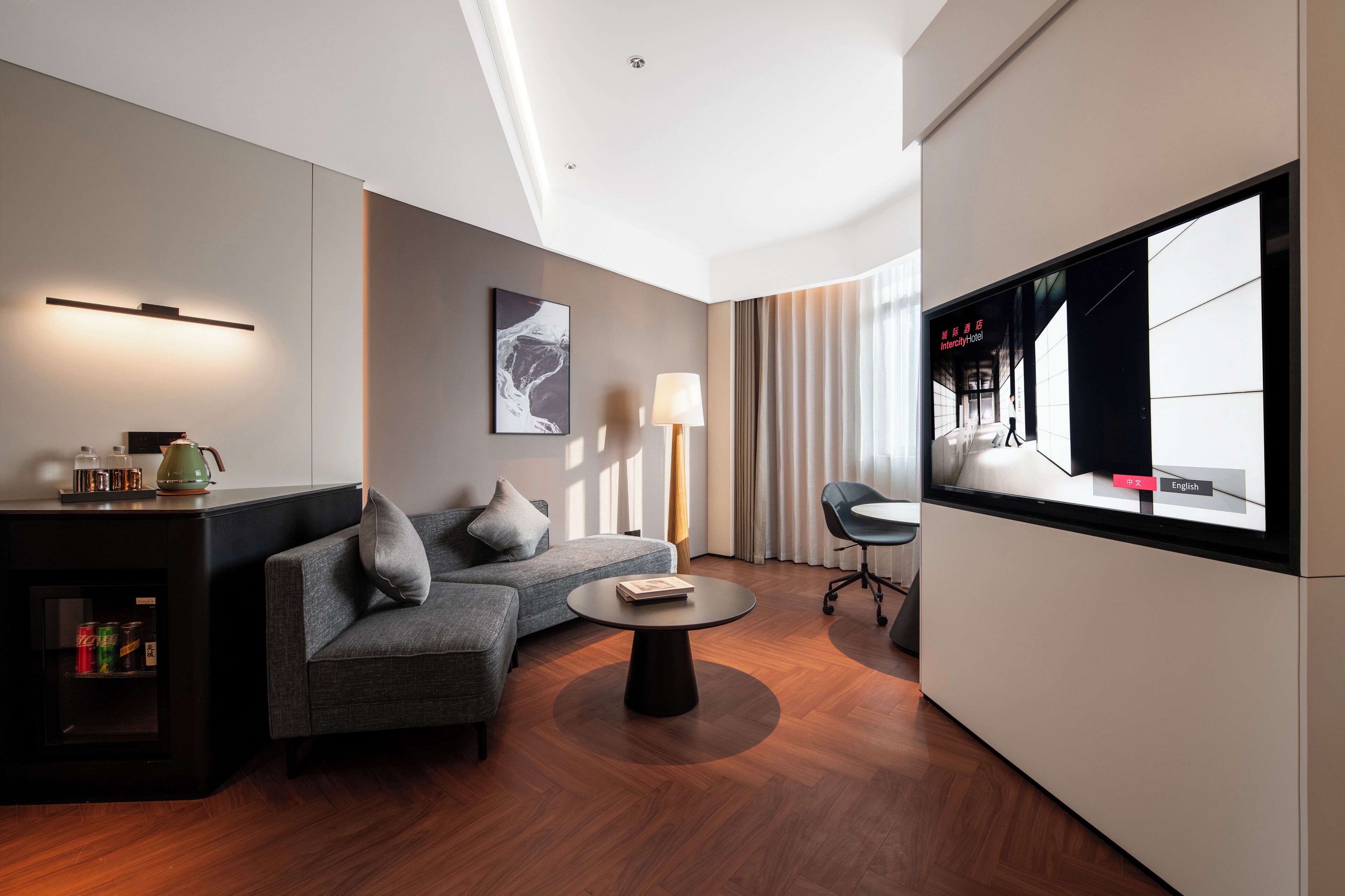 Una habitación de hotel moderna con sofá, una mesita, televisión y minibar.