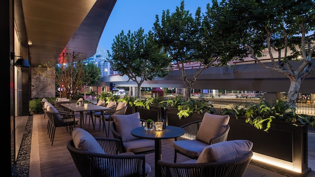 An outdoor seating area with tables and chairs, surrounded by plants and trees, overlooking a cityscape. - Intercity Shanghai Xujiahui (Shanghai)