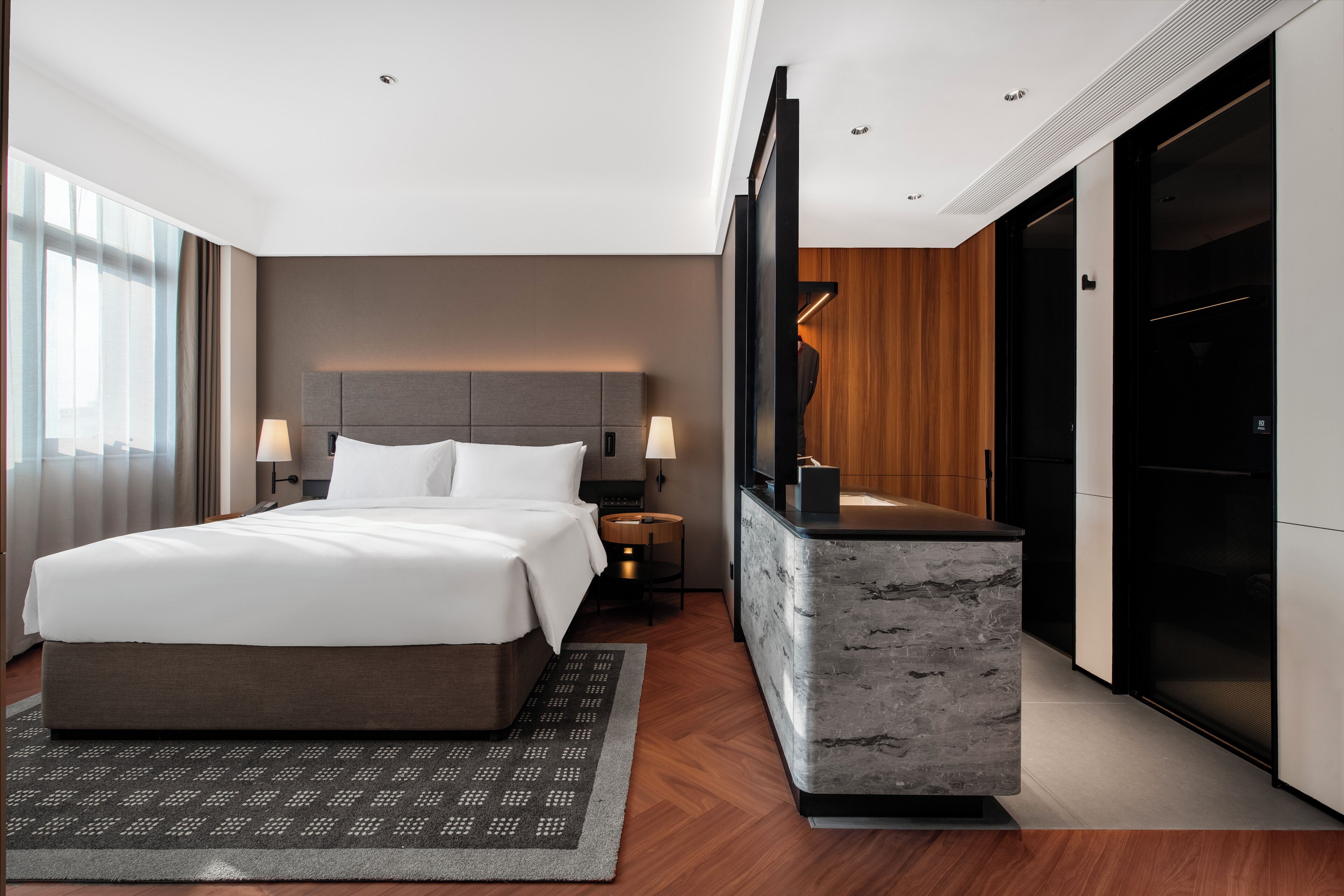Et moderne hotelværelse med en stor seng, fjernsyn, skrivebord og et klædeskab.