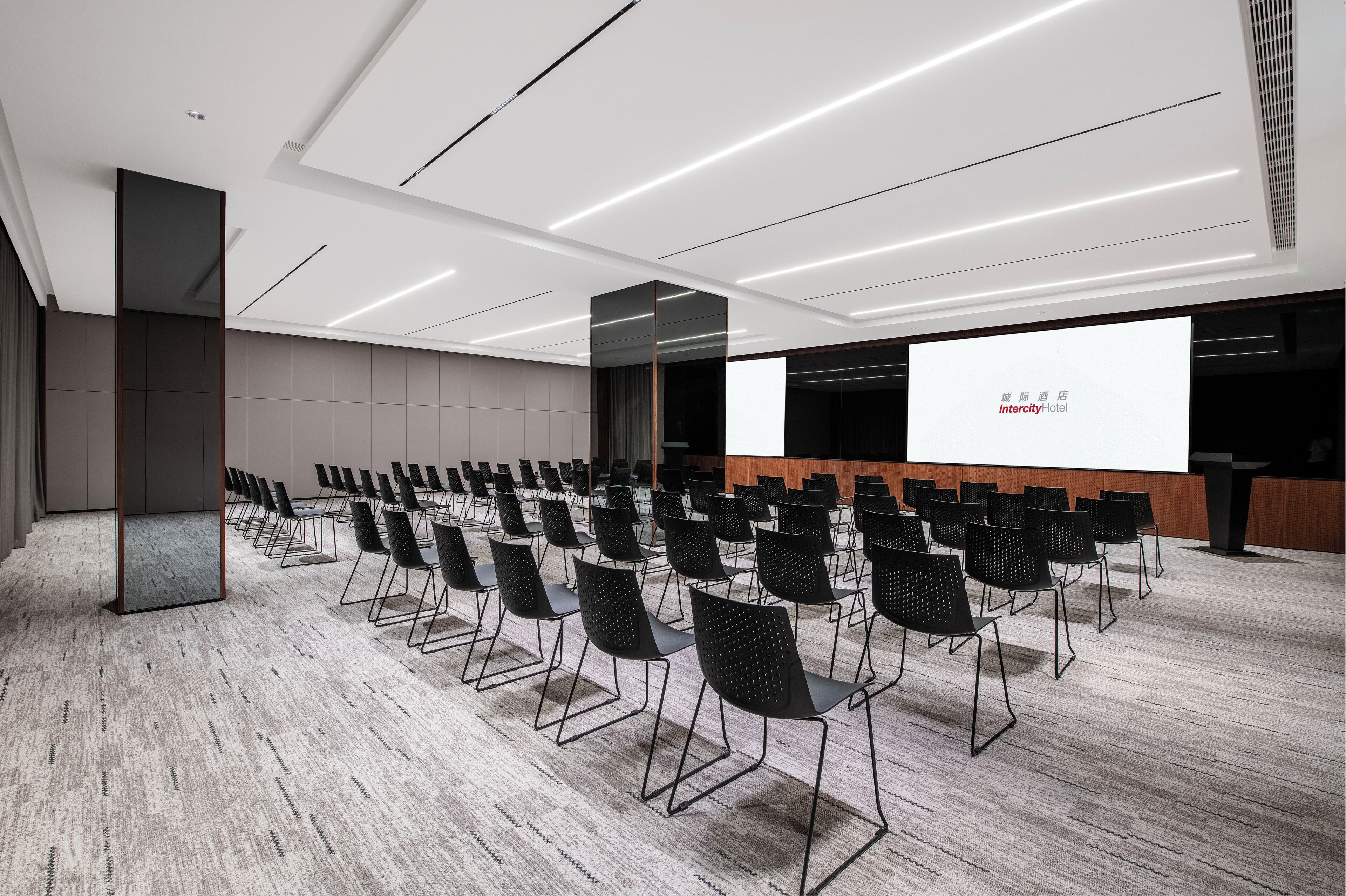 Un salón de conferencias con filas de sillas, una pantalla de proyección y un atril.