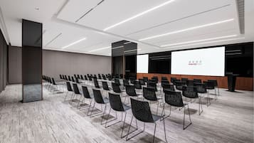 Un salón de conferencias con filas de sillas, una pantalla de proyección y un atril.