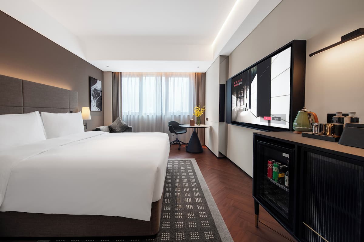 Una habitación de hotel con una cama grande, un escritorio con silla, televisor y minibar.