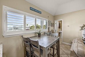 Un espace repas comprenant une table et des chaises, une plante en pot, une enseigne au-dessus des fenêtres et une vue sur l’extérieur.