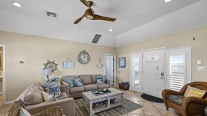 A spacious living room with a ceiling fan, a sofa set, a coffee table, wicker chairs, and a door with a window. - Relaxed Beach Getaway with Canal Views (Galveston)