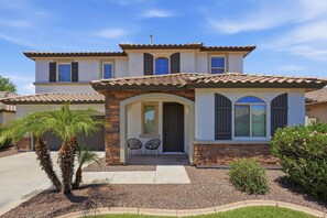 A two-story house with a tiled roof, a front porch with chairs, and a palm tree. - Family-Friendly 4BR Home, 30+ Night Stays -  Loft, Big Backyard (Gilbert)
