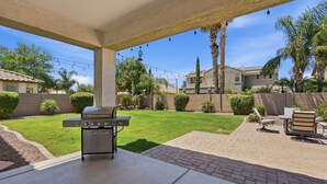 Eine überdachte Terrasse mit Grill, Gartenmöbeln und Blick auf einen gepflegten Rasen sowie angrenzende Häuser.