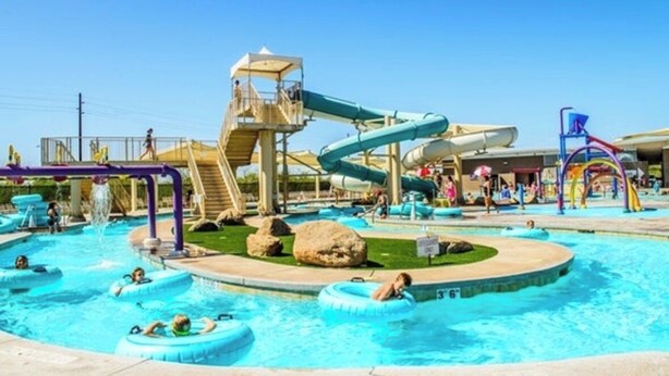 Ein Wasserpark mit mehreren Rutschen und Pools, darunter ein zentral gelegener Kreispool mit aufblasbaren Ringen.