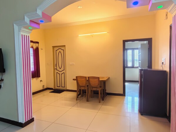 A dining area with a table and chairs, a door with a decorative design, and a refrigerator. - MG Elite Residency (Puducherry)