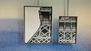 A hotel room with a bed, two white pillows, and two framed black and white photographs of a bridge on the wall.