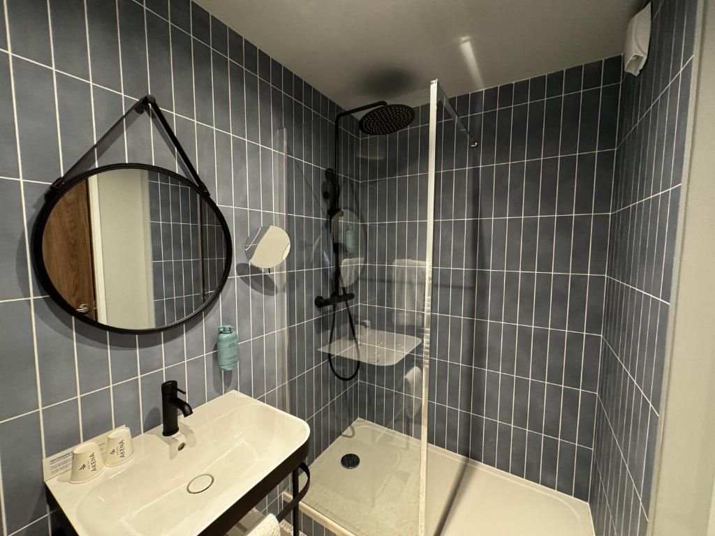 Baño con lavamanos, espejo, ducha y paredes de cerámica.