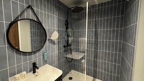 A bathroom with a sink, mirror, shower, and tiled walls.