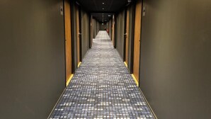 A hotel hallway with a checkered floor, doors on both sides, and a fire extinguisher on the wall. - Akena Serris (Serris)