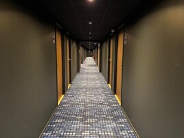 Un pasillo de hotel con suelo a cuadros, puertas a ambos lados y un extintor en la pared.