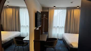 Habitación de hotel con dos camas individuales, un escritorio con silla, un televisor y un perchero.