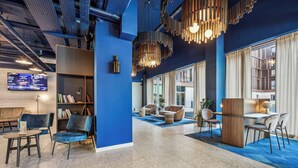A modern lobby with a blue accent wall, a bookshelf, seating areas, and a large window providing natural light. - Akena Serris (Serris)