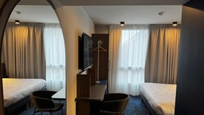 A hotel room with two single beds, a desk with a chair, a TV, and a coat rack. - Akena Serris (Serris)